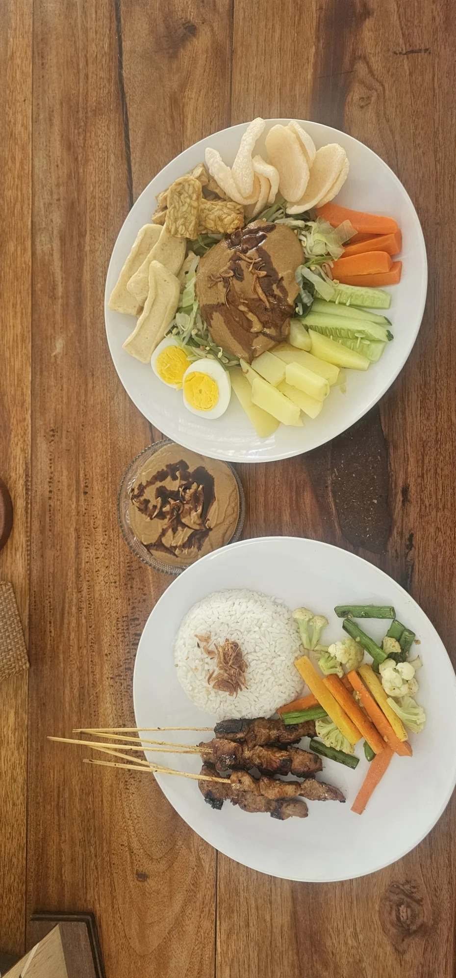 Two plates of Indonesian food served on a wooden table
