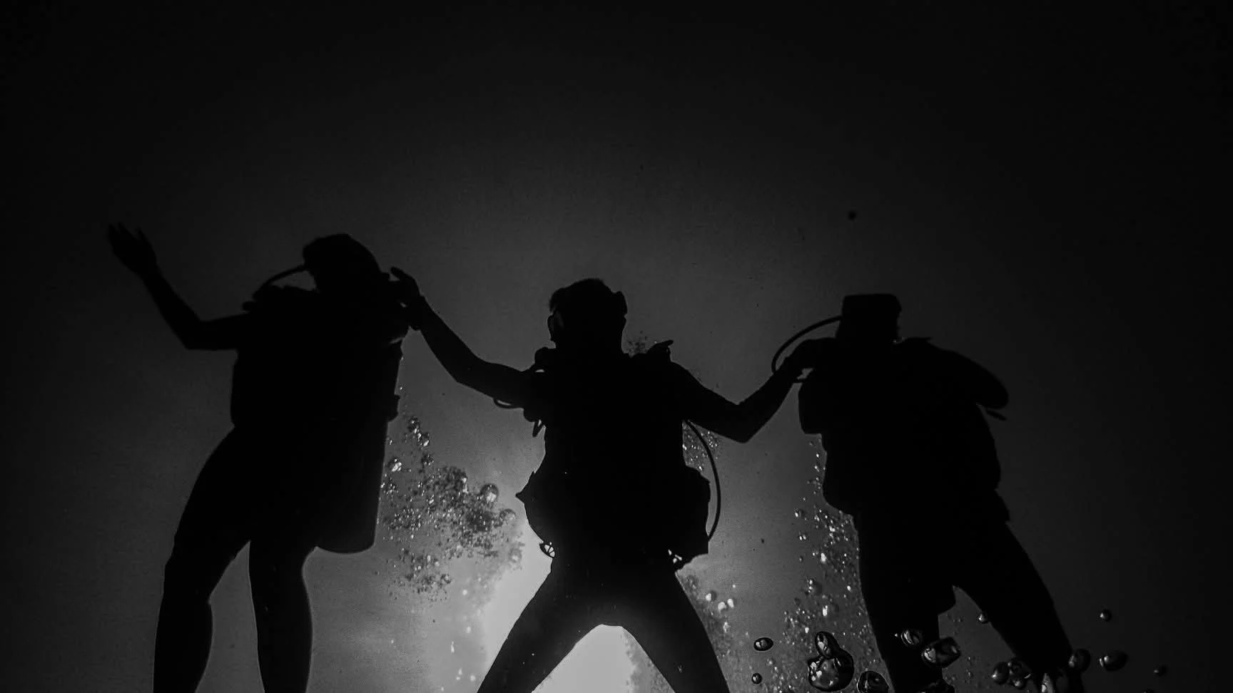 Three divers silhouetted above the USAT Liberty wreck